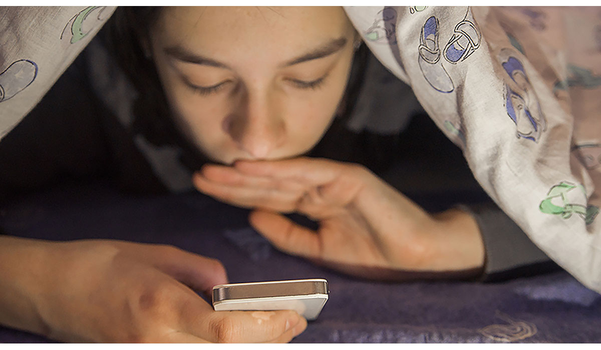 Teen Lying On Front In The Bed And Using Smartphone