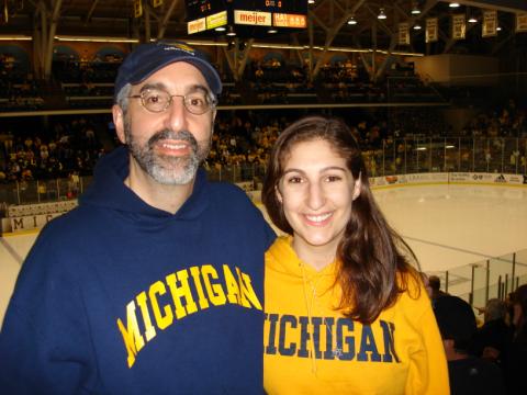 David Gutmann, left, in a blue Michigan sweatshirt, poses with his daughter, right, who is in a maize Michigan sweatshirt. They are at Yost Arena.