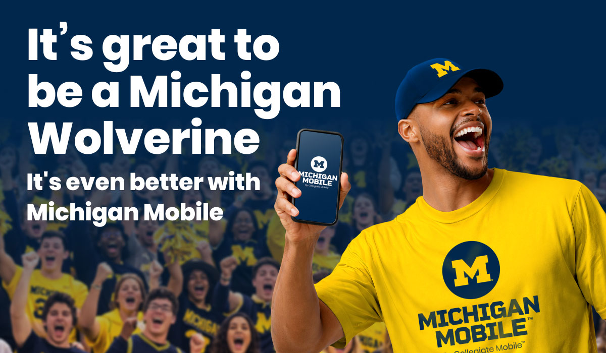 A smiling person in a maize Michigan Mobile shirt and navy Michigan hat holds up a phone featuring the Michigan Mobile logo in front of a cheering crowd in Michigan apparel. Promotional text says, "It's great to be a Michigan Wolverine. It's even better with Michigan Mobile."