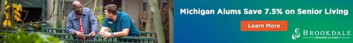 Two people chat near a green railing in a leafy outdoor setting. The right side has a blue and green banner advertising a 7.5% senior living discount for Michigan alumni, along with a Learn More button and Brookdale Senior Living logo.