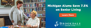 A caregiver chats with a senior citizen in a library-like setting. The right side has a blue and green banner advertising a 7.5% senior living discount for Michigan alumni, along with a Learn More button and Brookdale Senior Living logo.