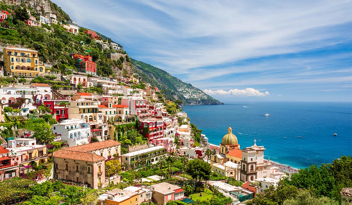 A colorful coastal town sits in green mountains along vibrant blue waters.