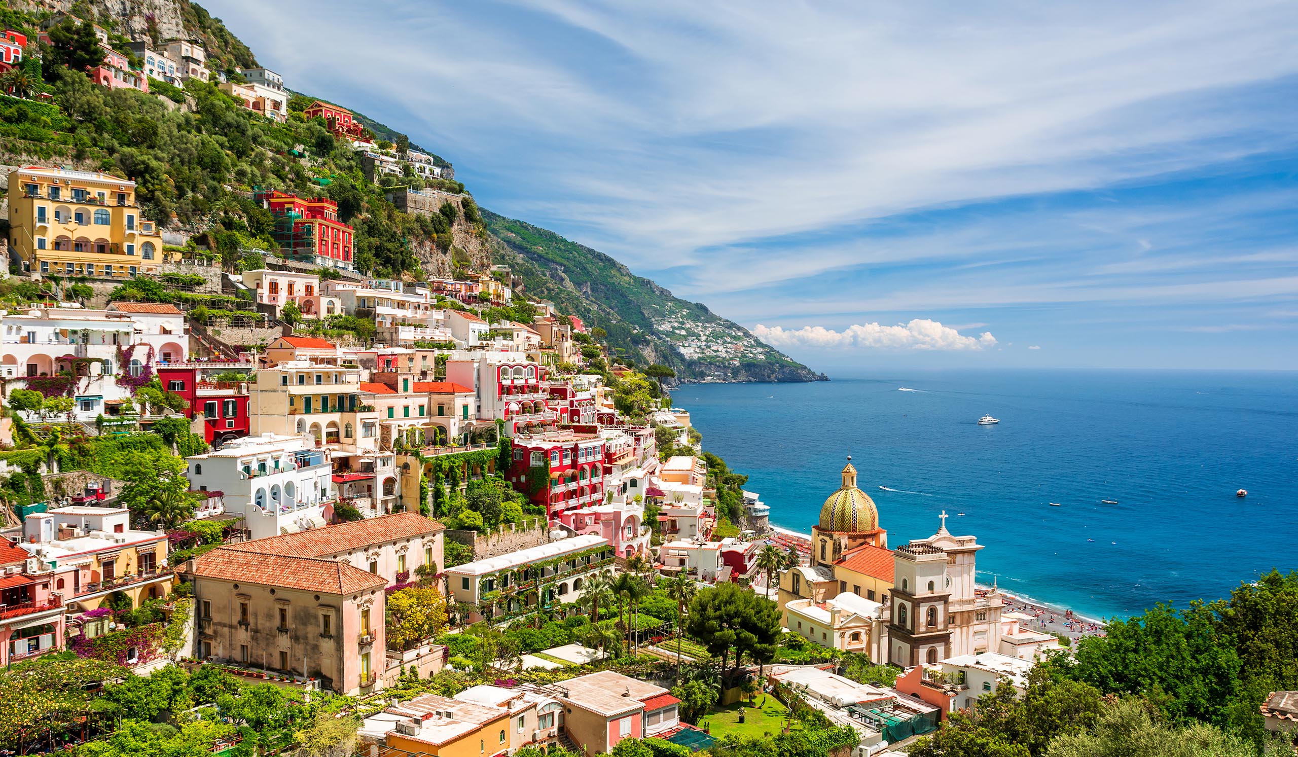 A colorful coastal town sits in green mountains along vibrant blue waters.