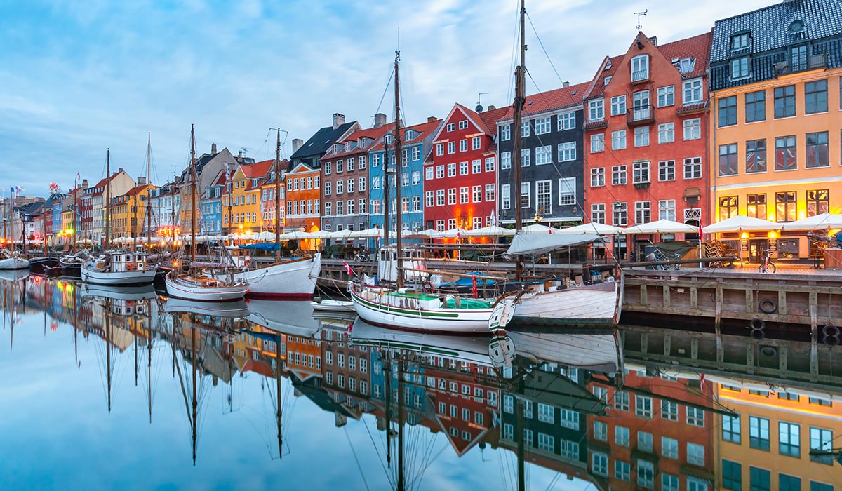 Colorful buildings line a canal with boats docked along the water, reflecting in the calm surface.