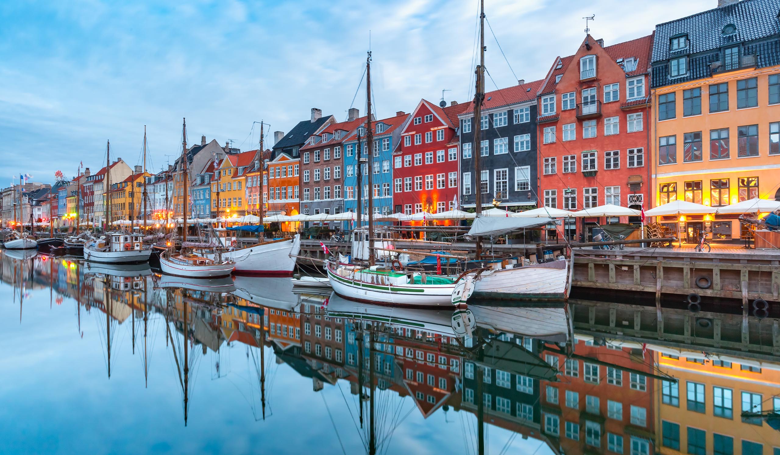 Colorful buildings line a canal with boats docked along the water, reflecting in the calm surface.