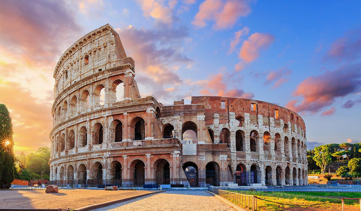 The Colosseum stands in Rome under a colorful sunset sky.