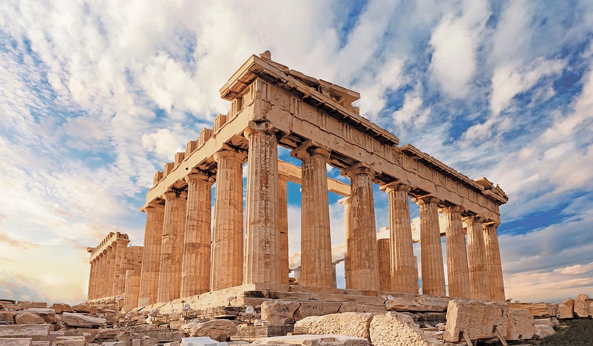 Ancient stone columns of the Parthenon stand under a partly cloudy sky.