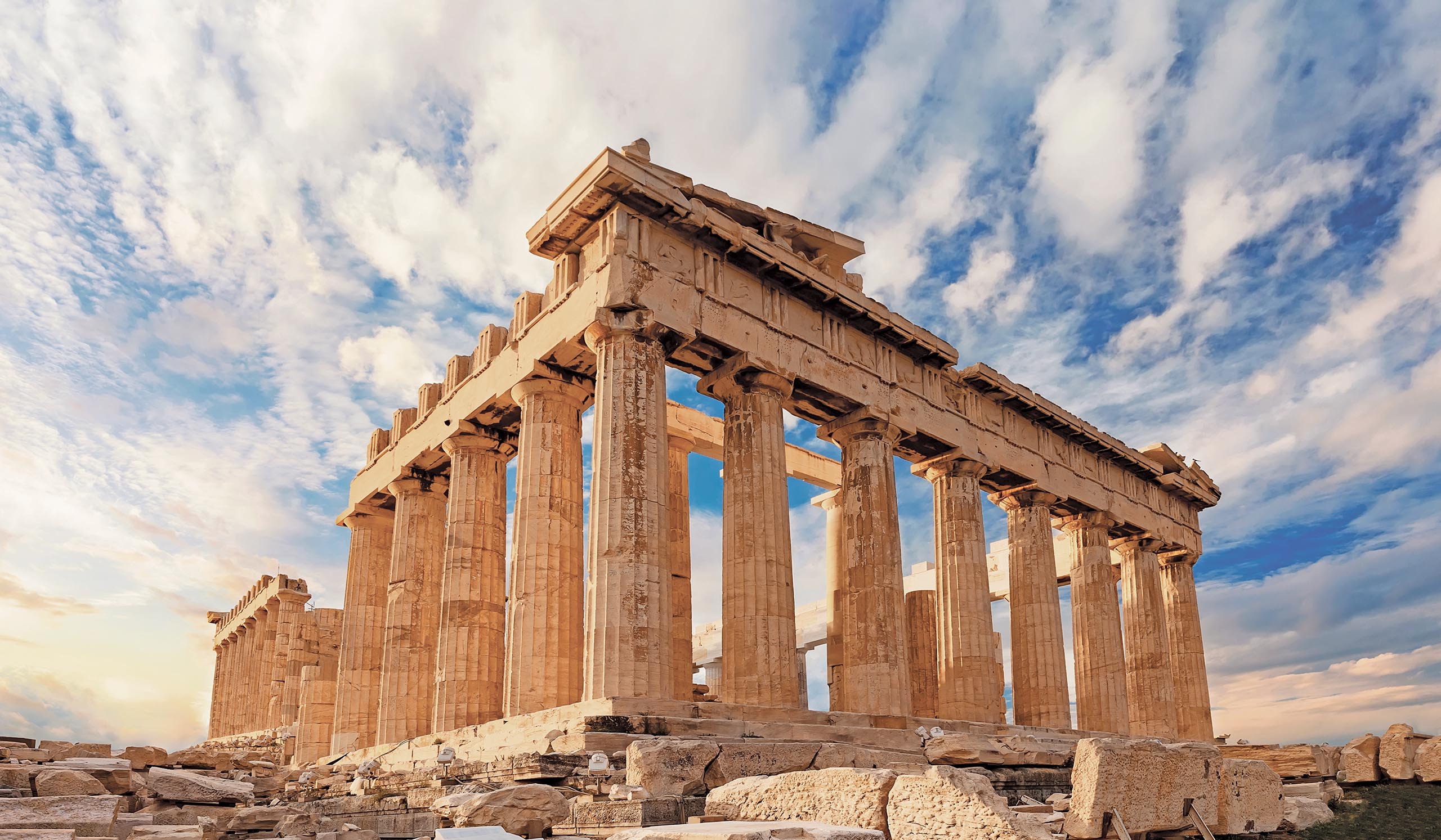Ancient stone columns of the Parthenon stand under a partly cloudy sky.