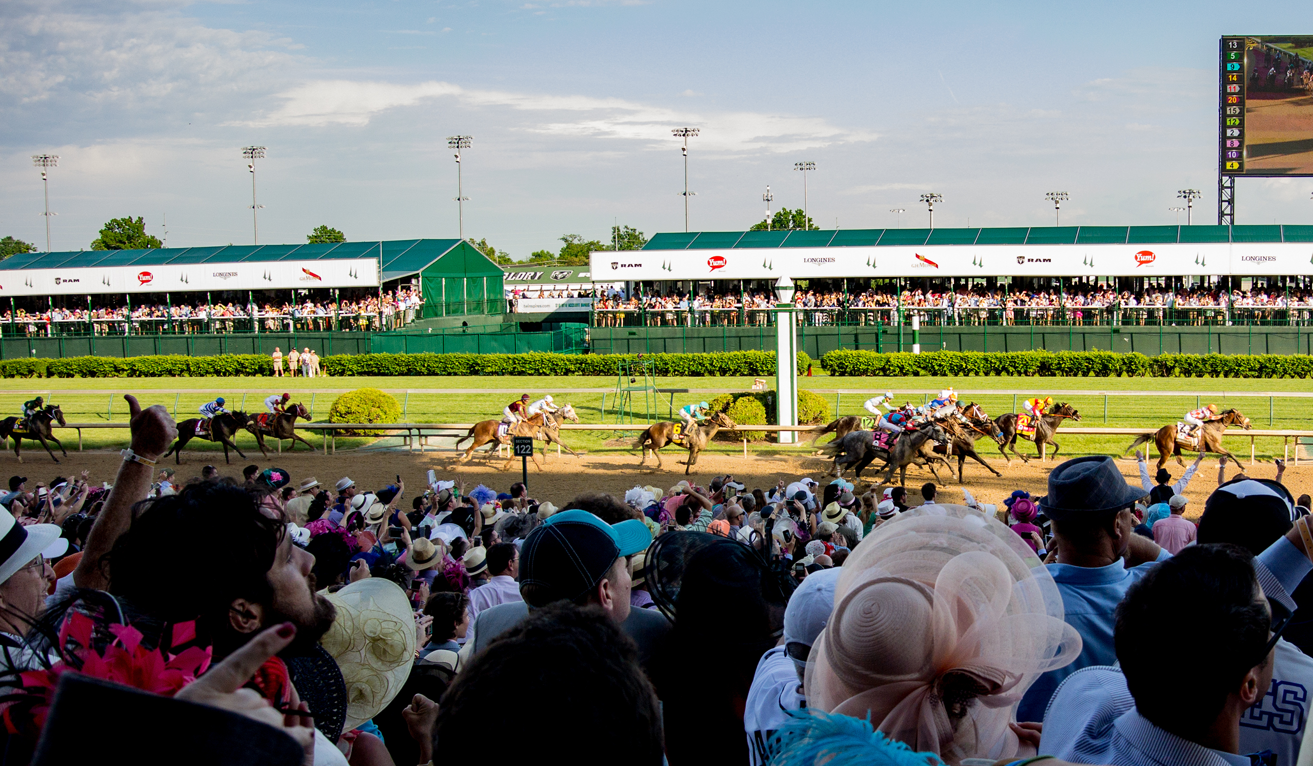 Fans in the crowd at Churchill Downs watch as the horses run on the track in the Kentucky Derby.