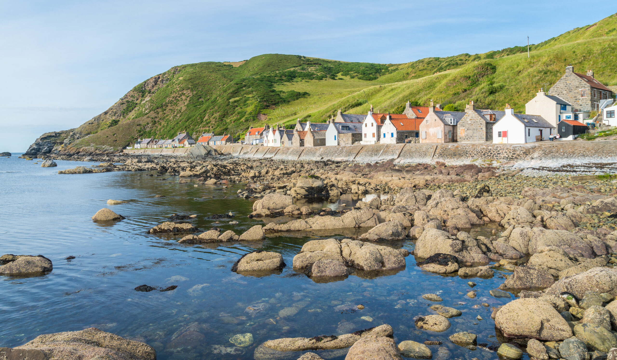 Dramatic coastal landscape at sunset with rugged cliffs and a natural rock arch rising from the sea, framed by grassy hills glowing in warm, golden light.