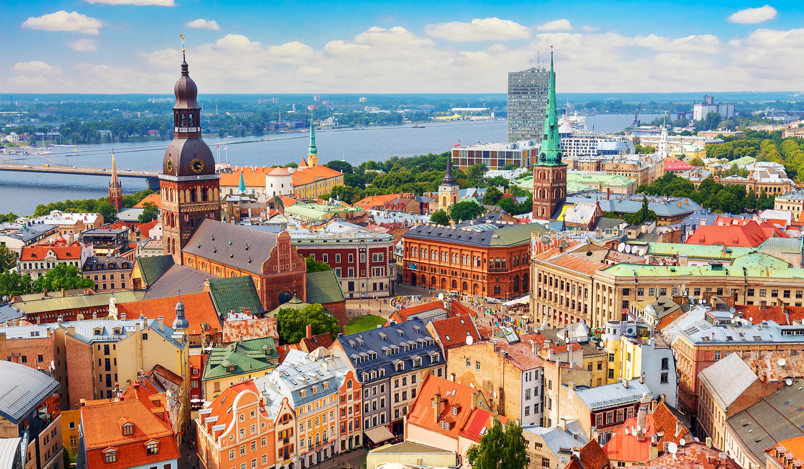 Aerial view of a colorful European city with historic buildings and church spires, including a large cathedral with a dark dome, set beside a wide river.