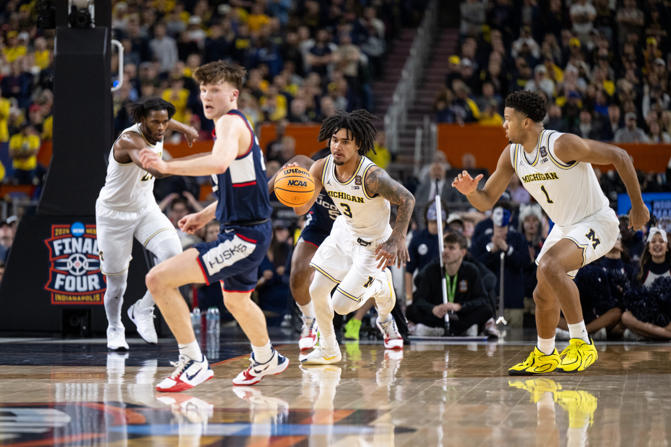 A Michigan basketball player takes the ball down the court towards the camera against Uconn.