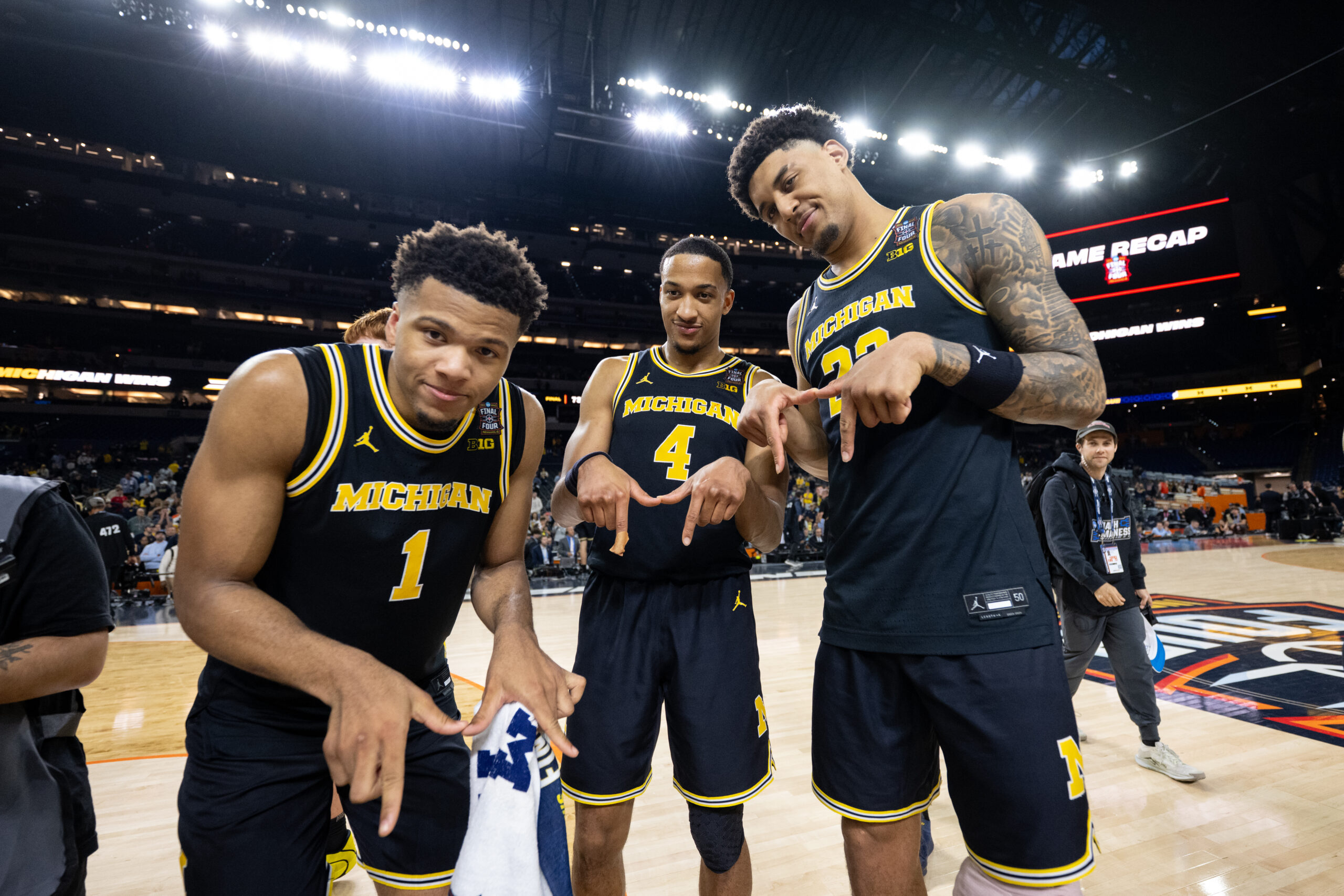Three Michigan basketball players pose with their fingers in the shape of Ms.