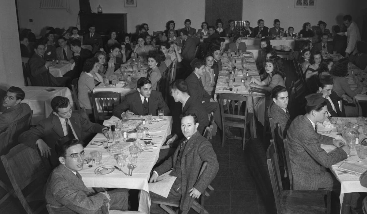 A large gathering of students sit at dining tables, dressed in nice clothes for a meal.