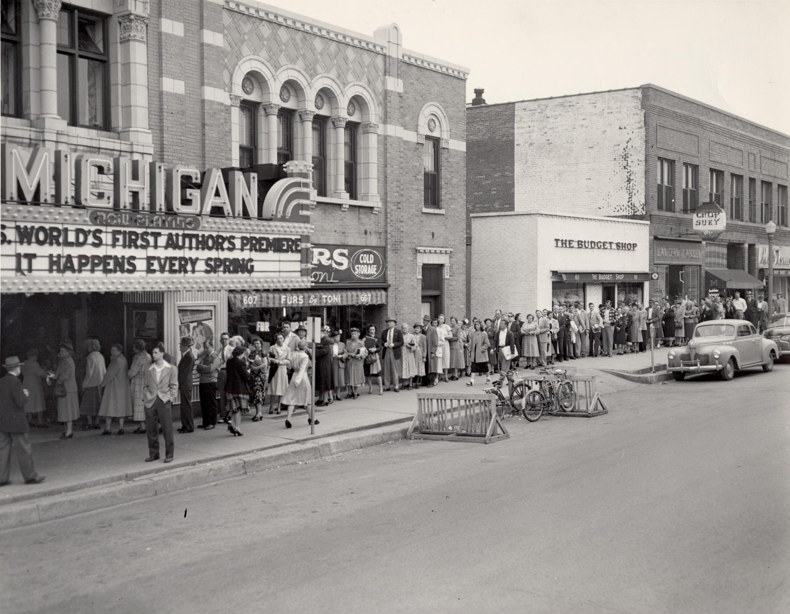 People wait outside the Michigan Theater. Bicycles and vintage cars line the street.