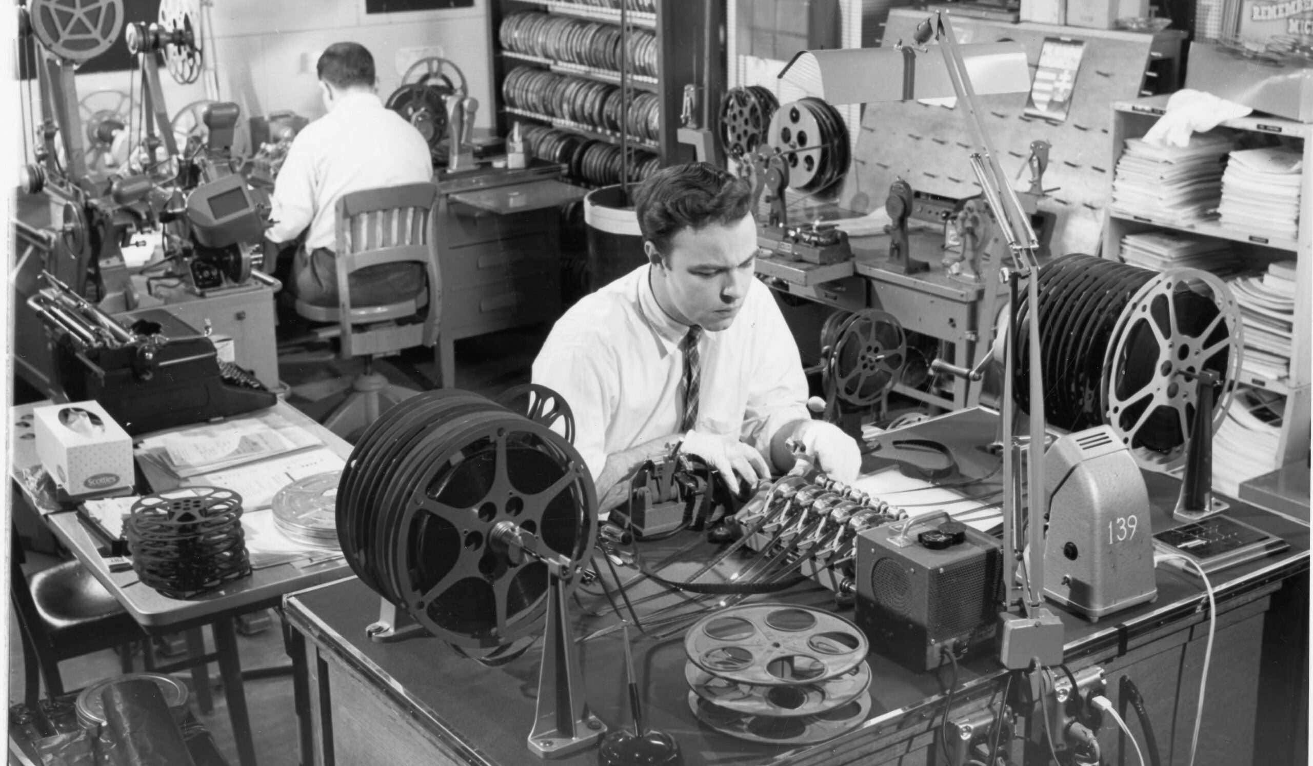 A black-and-white photo highlights U-M alums editing film together, surrounded by reels and papers in a vibrant, collaborative space.