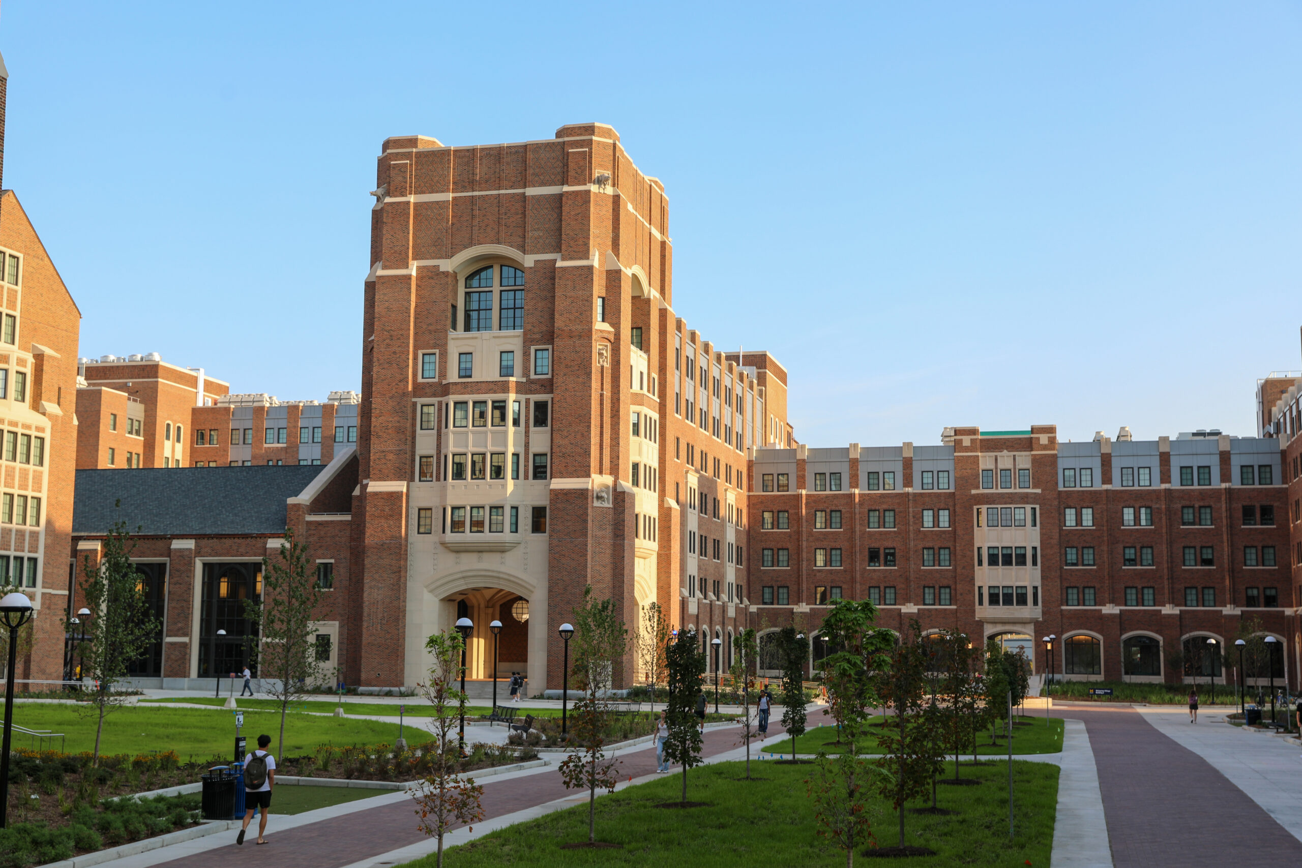 A large brick university building with many windows, an archway entrance, and walkways bordered by green lawns.