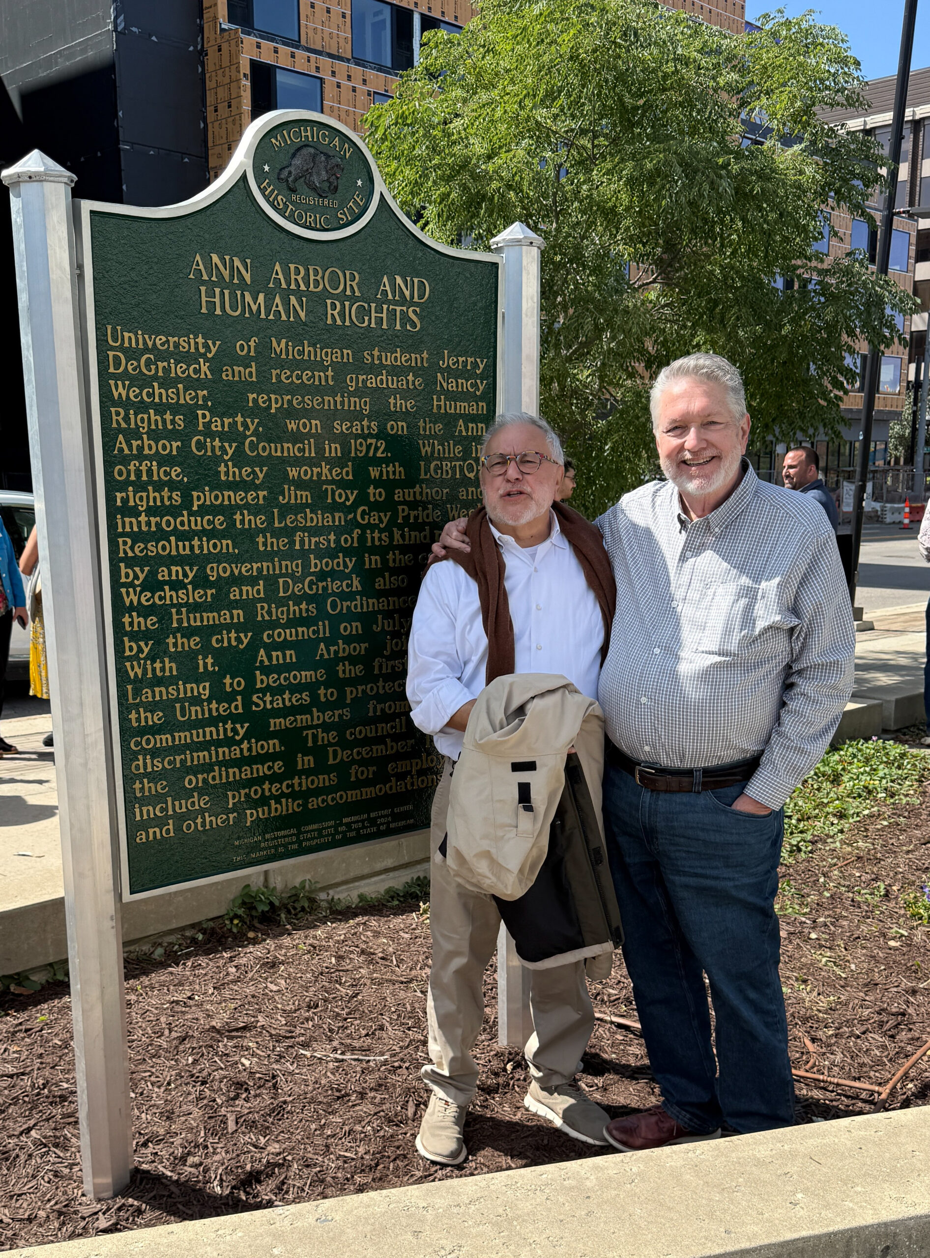Two people stand with their arms around each other next to an Ann Arbor and Human Rights historic marker.