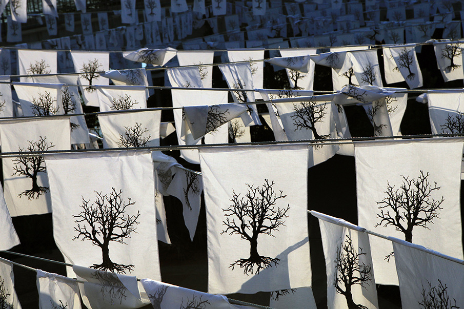 Multiple clotheslines outdoors display white cloths with black tree designs, closely filling the area.