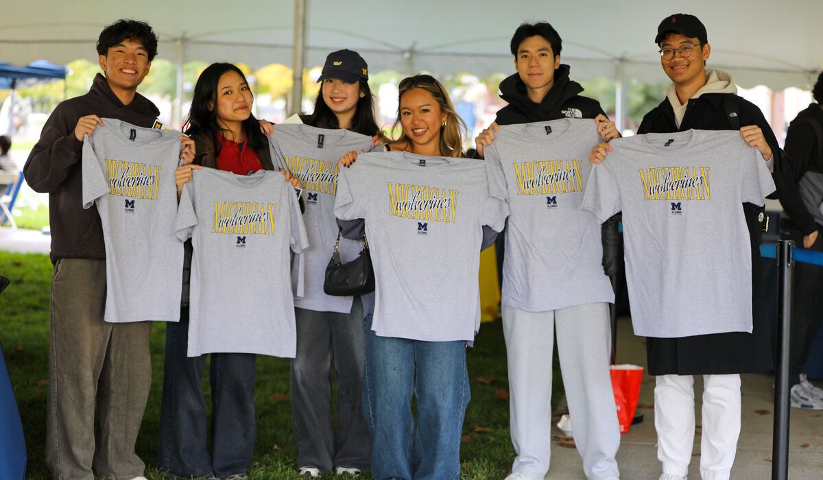 A group of people hold up grey shirts that say Michigan Wolverines on it.