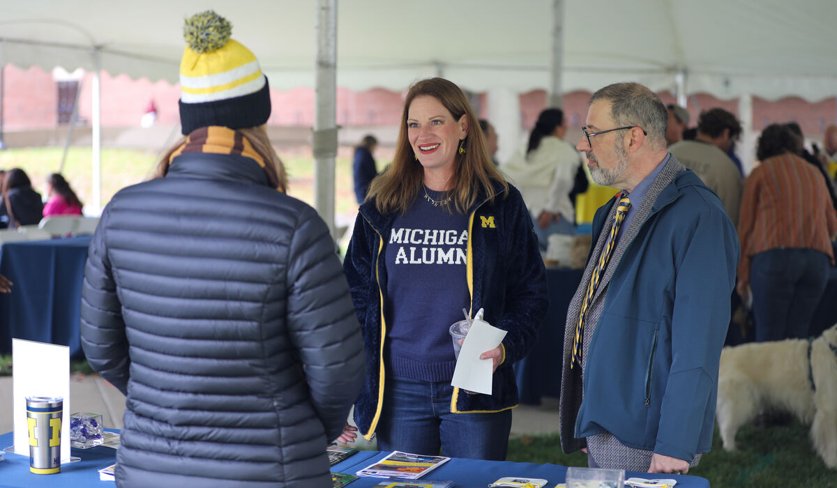 A man and a woman wearing michigan clothing talk to a vendor at an event.