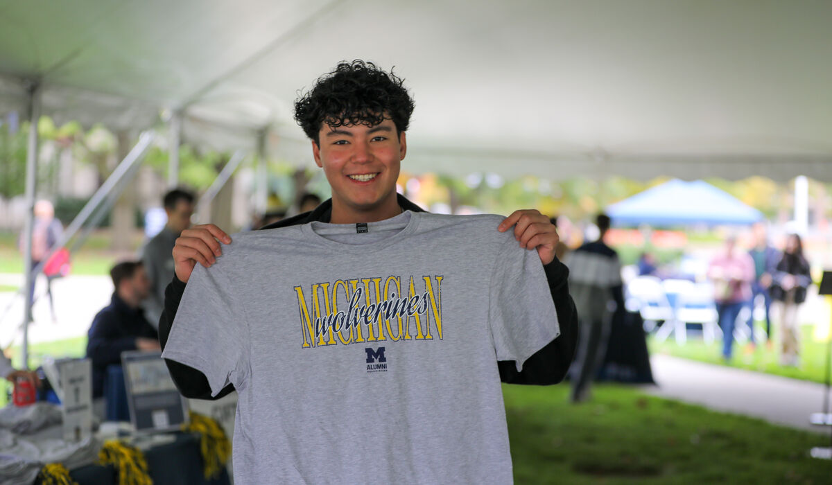 A student holds up a grey shirt that says Michigan Wolverines on it.