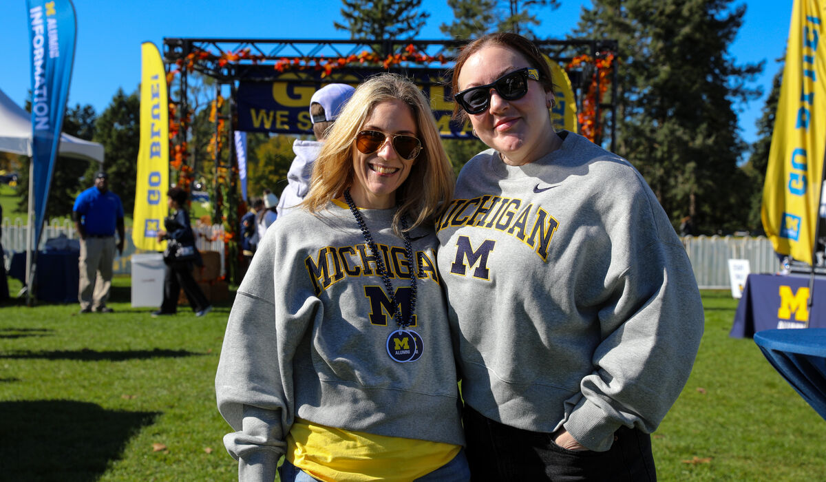 Two people wearing grey Michigan sweatshirts smile for a camera.