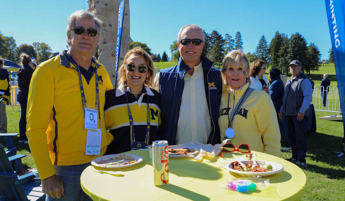 A group of four people pose for a photo in front of a rock climbing wall. There is food on the table in front of them.