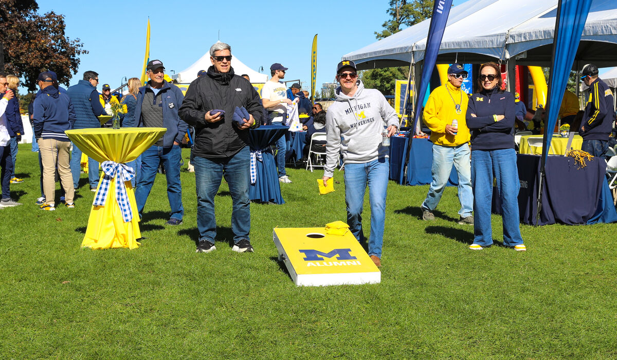 A man tosses a bean bag as part of a game during a tailgate