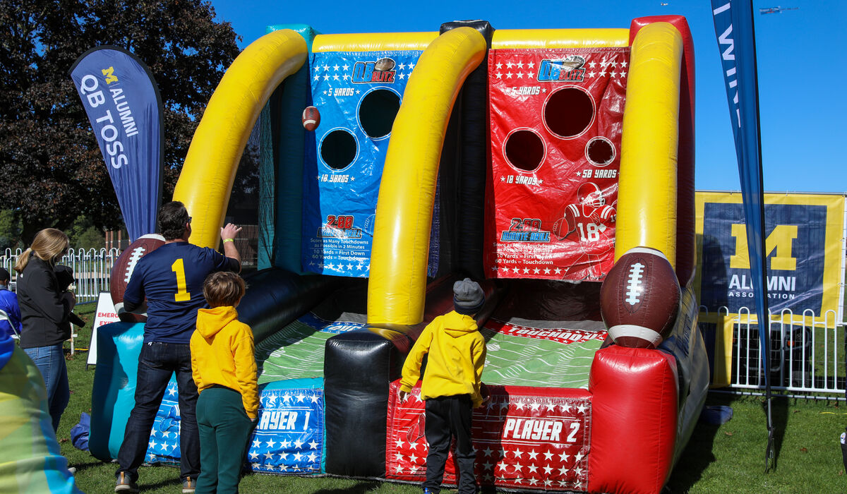A man and a child throw footballs into an inflatable game.