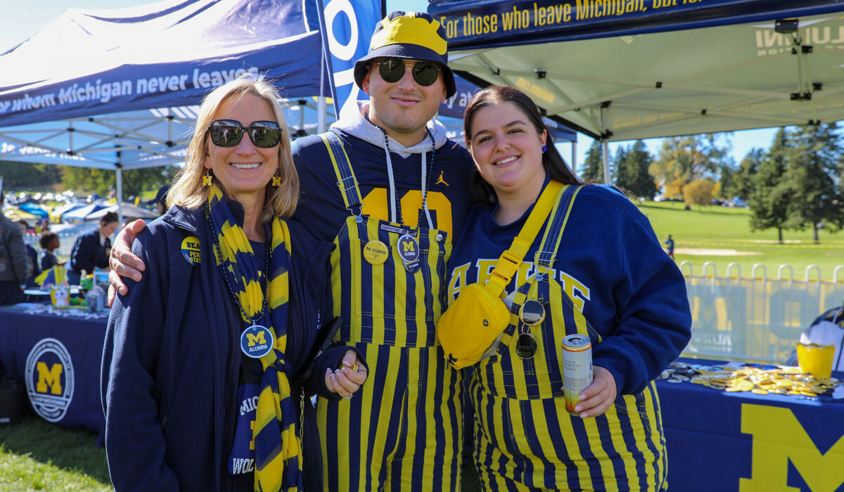 Three people pose for a camera. Two are wearing maize and blue stripped overalls.