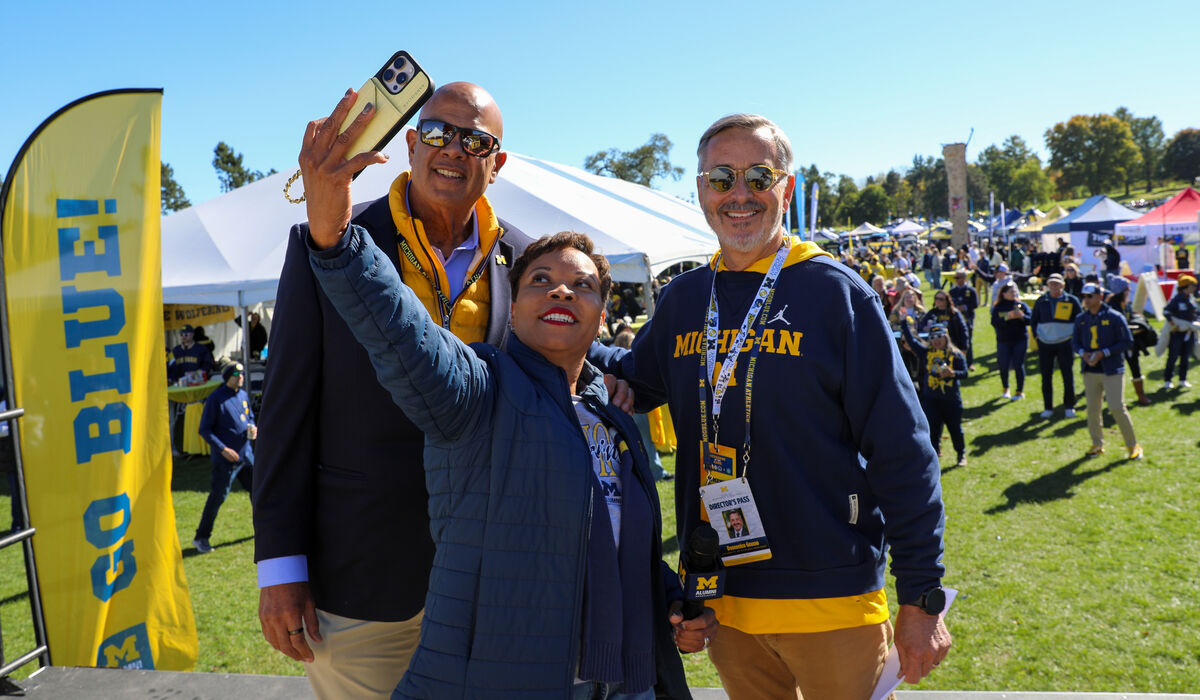 A woman holds up a phone and takes a self with two men