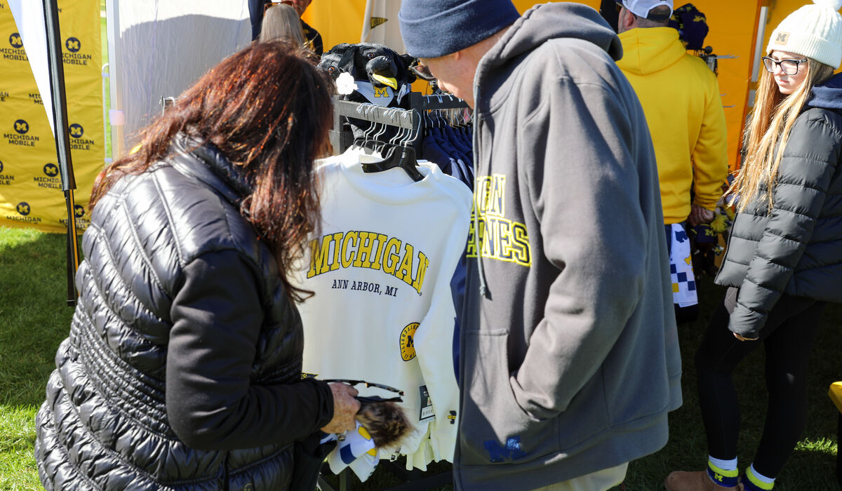 Two people look at a white shirt on a clothes rack that reads Michigan Ann Arbor