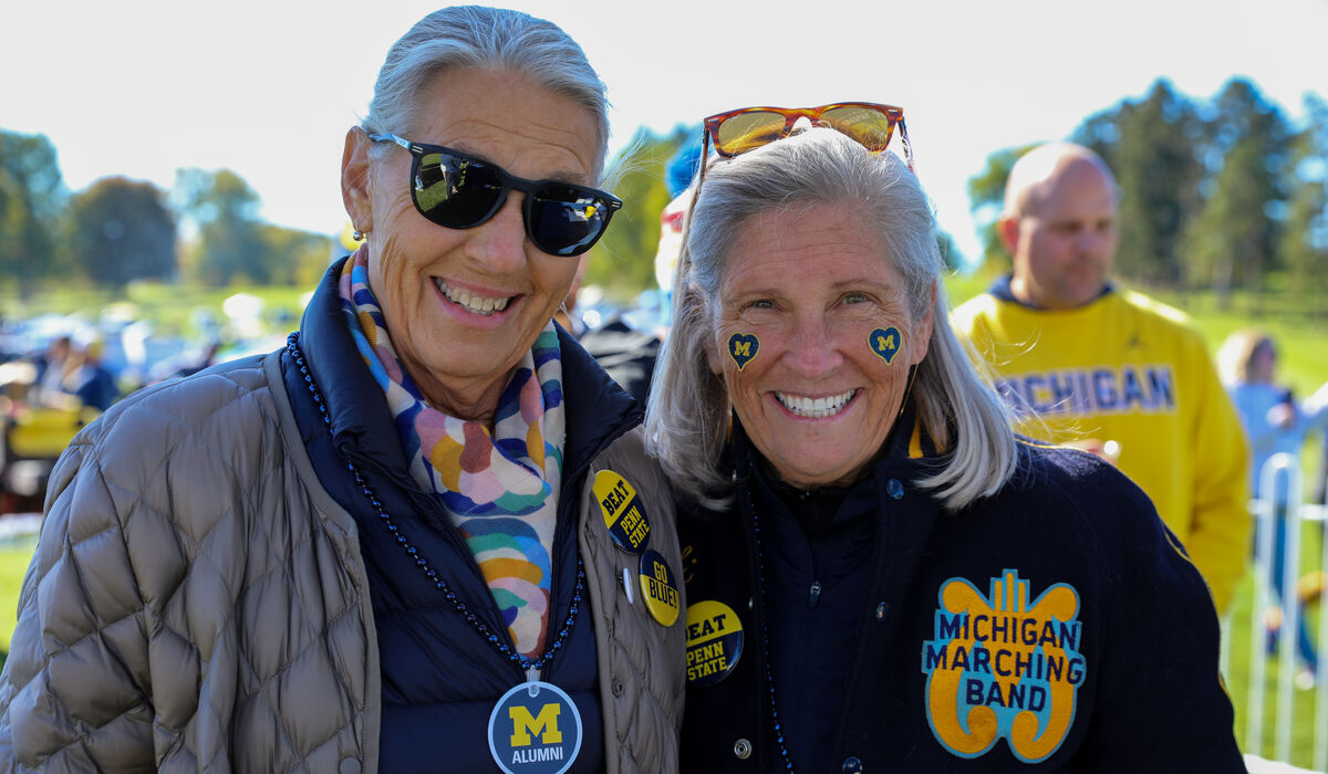 Two women pose for a photo. one is wearing a vintage michigan Marching band jacket