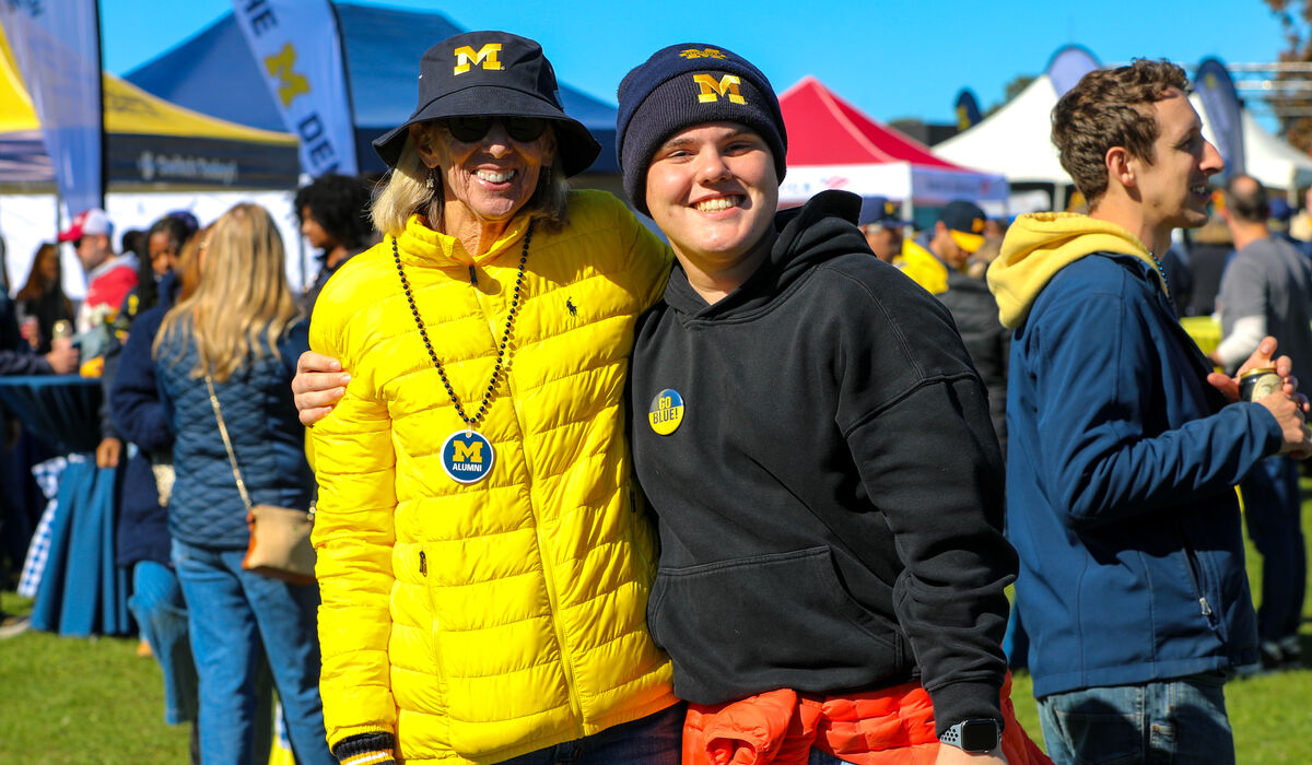 Two individuals stand in a field at a tailgate.