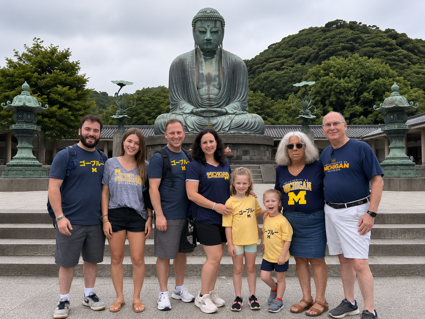 Nine people pose in front of a large Buddha statue, all wearing University of Michigan clothing.