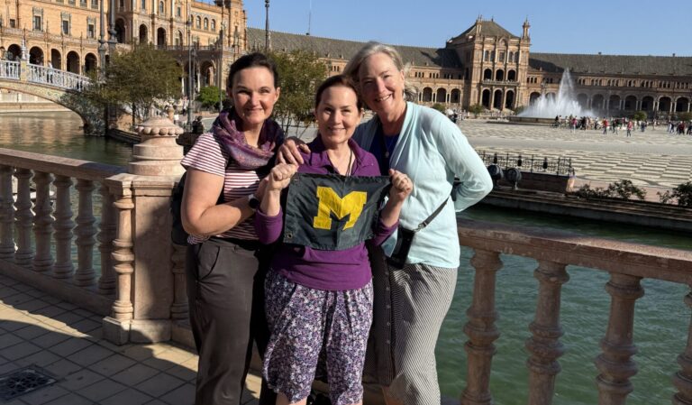 Three people stand together by a balustrade at Plaza de España in Seville, Spain, on a sunny day.