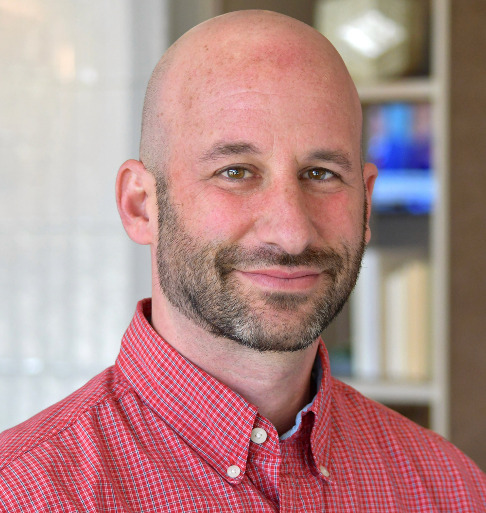 Mike Shriberg is pictured wearing a red button up shirt. 