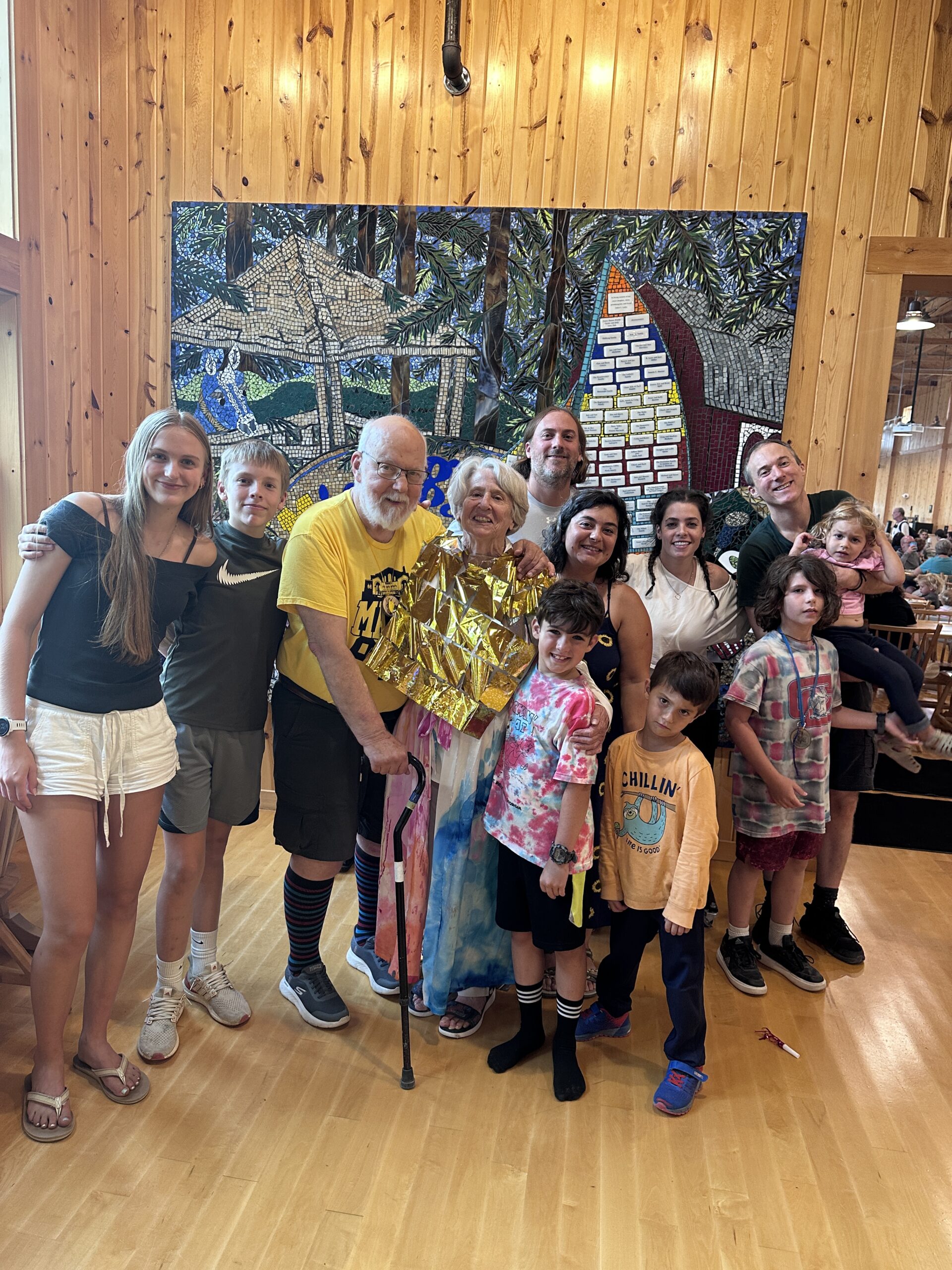 A group of people, including adults and children, stands smiling indoors in front of a colorful mural.
