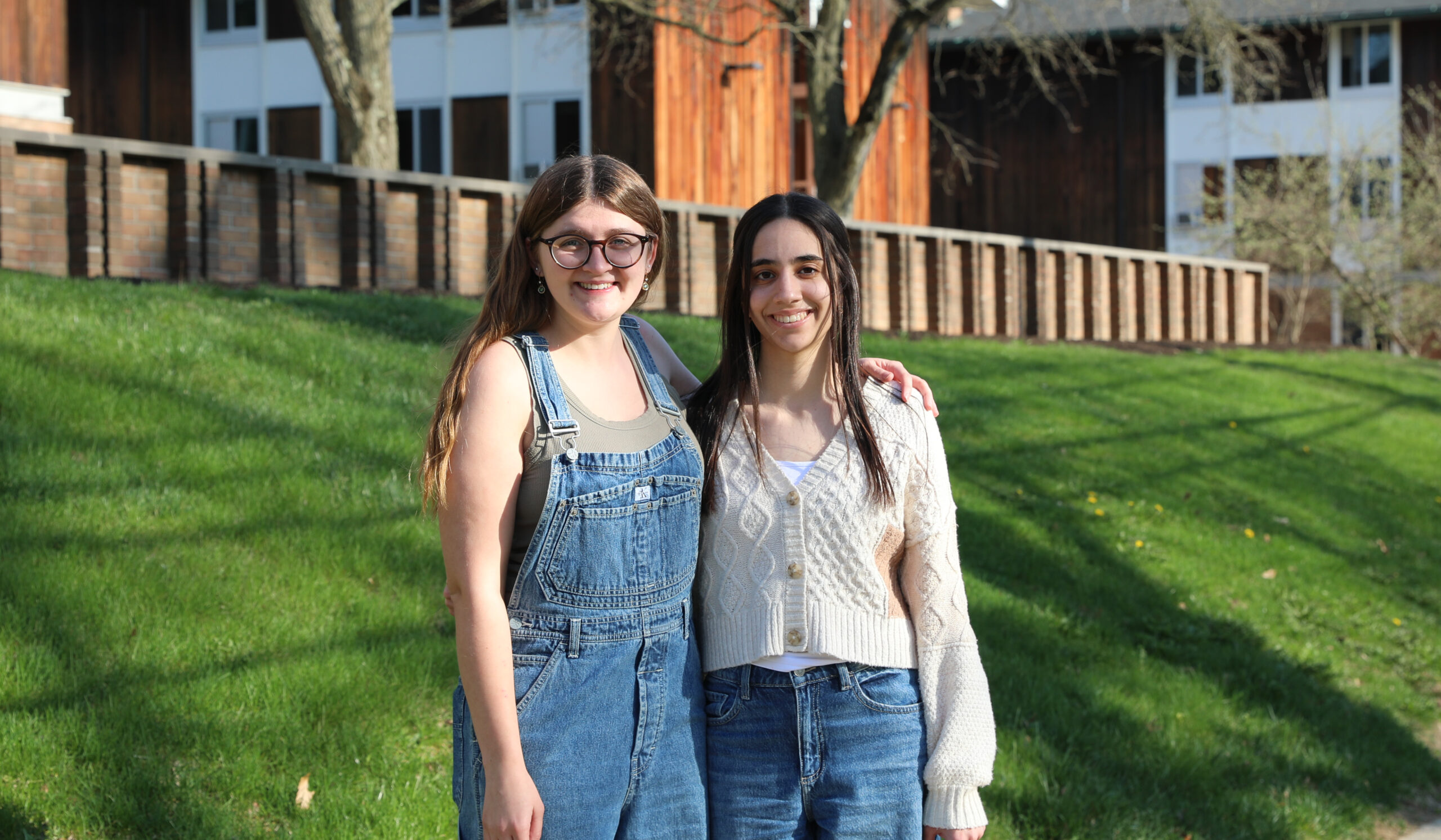 Madison Quinn, left in overalls and a green tank top, puts her arm around Emma Mastroianni, right, in jeans and a cream sweater. The two stand outside of Oxford Houses.