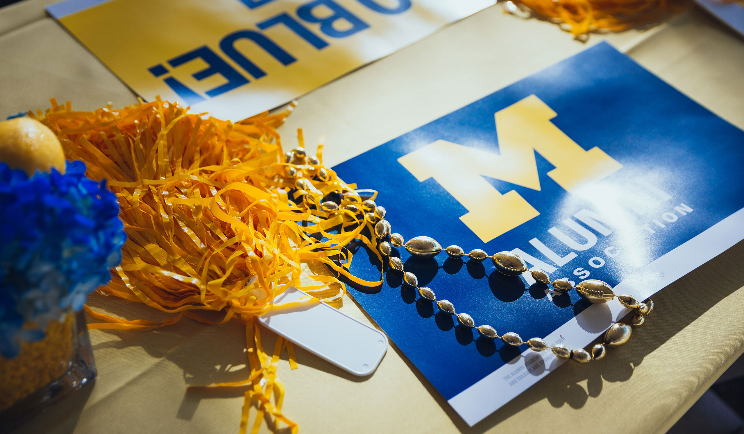 An Alumni Association sign next to football-shaped beads and a maize pom-pom