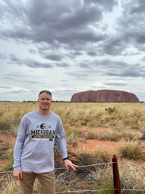 Aaron Brooks, ’98, gives a “Go Blue!” from near Uluru in Australia recently. It wasn’t that far of a trip, as he serves as the U.S. Senior Defense Official/Defense Attache in the U.S. Embassy in Canberra.