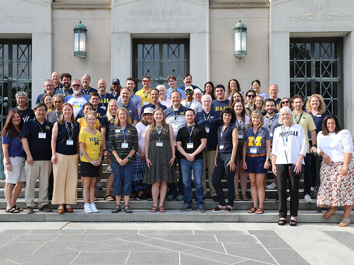A large group of Michigan alumni club and affiliate leaders poses for a photo on the front steps of the Rackham Graduate School building.