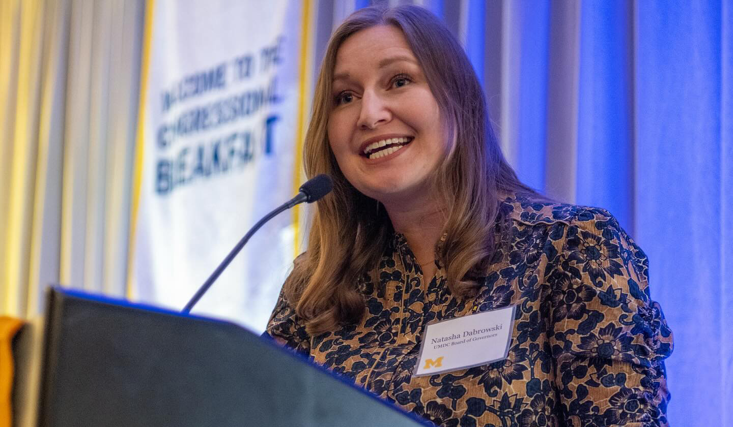 A woman speaks into a microphone at a podium. Behind her there's a sign that says "Welcome to the Congressional Breakfast"