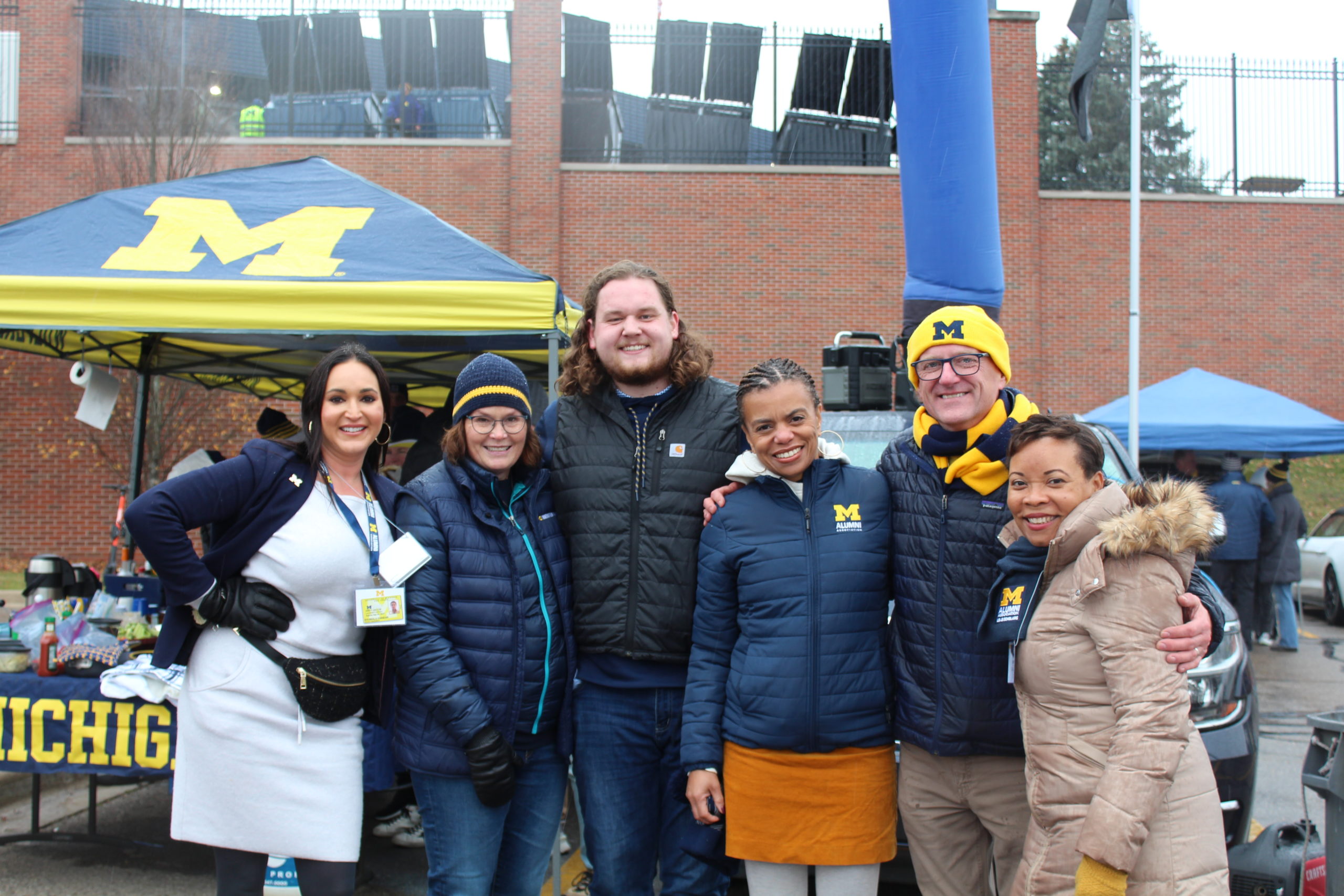 Corie Pauling poses at a Big House tailgate with Wendell Brooks, his family, and two members of the Alumni Association staff.