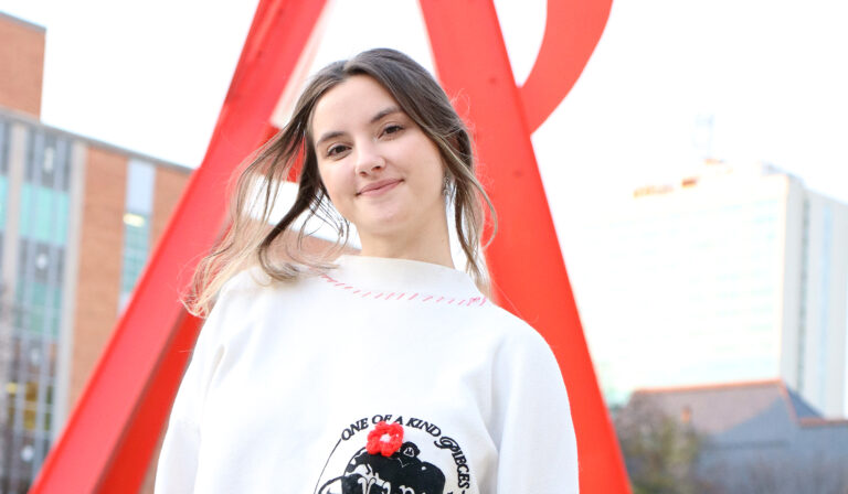Daphne Matter, wearing a VIPs sweater, poses in front of an UMMA sculpture on campus.