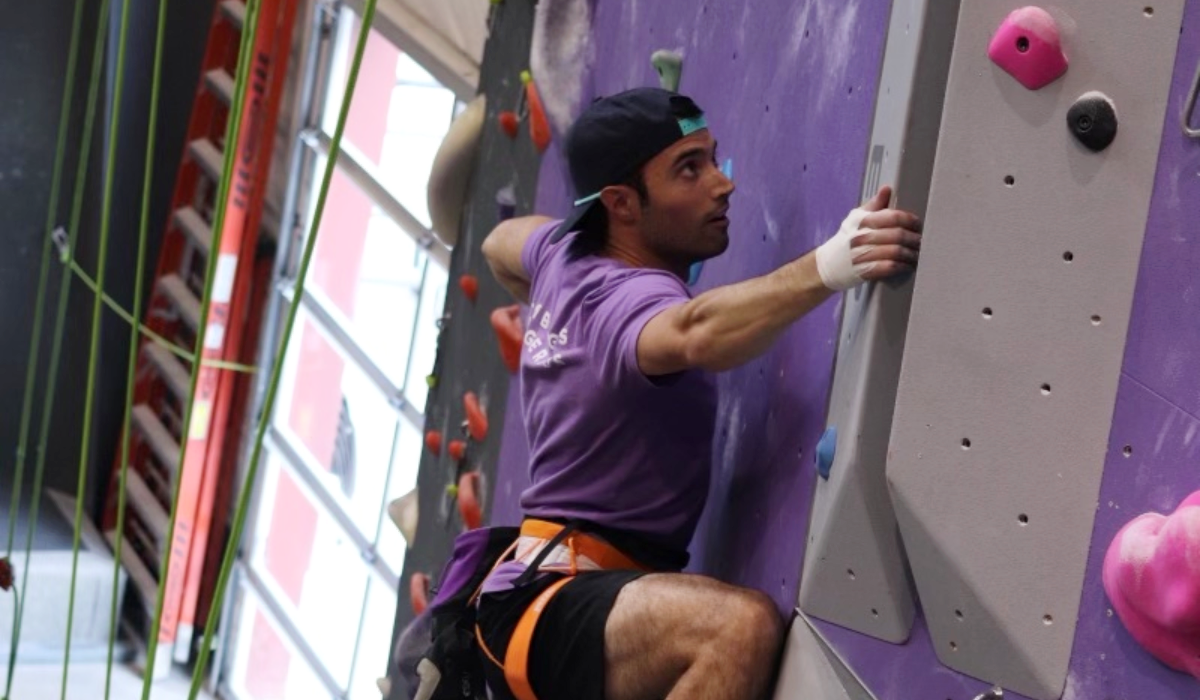 Dino Ruggeri in a purple shirt, rock wall climbing on a purple and grey rock wall at Dyno Detroit.