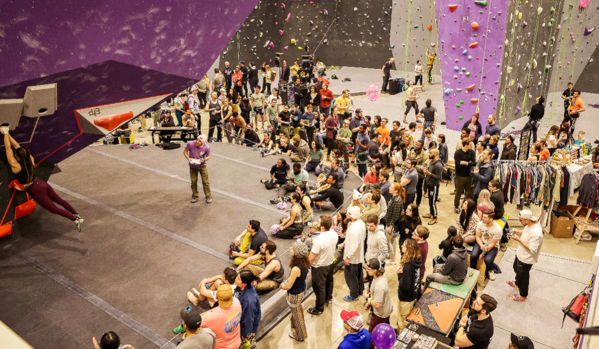Taken from above, a crowd of people gather to watch an indoor rock climbing demonstration at Dino Detroit.