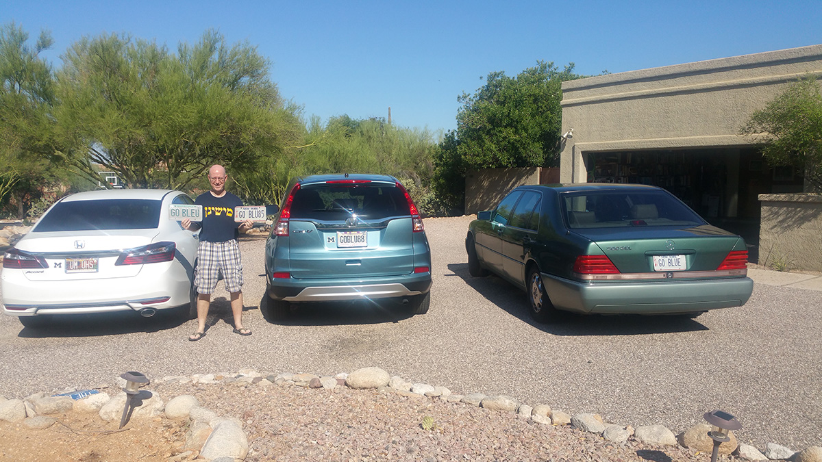 Doug Levy, ’85, in Tucson, Arizona, loves his Maize and Blue license plates, hence the GO BLU85 in his left hand. The UM UHS plate (left car) stands for U-M and University High School, which both his daughters attended. His wife, Nanci Ogur Levy, ’88, drives the car with the GOBLUE88 plate (middle car), while the GO BLUE plate (right car) is an expired New York plate he temporarily slapped on his vintage Mercedes for this photo. Normally, the Mercedes bears a UMICH85 plate (not pictured), though it once displayed the now expired GO BLEU plate in his right hand—his second choice when he learned GOBLUE was taken in Arizona. Levy’s friend Bruce Zenkel, ’52, previously owned the New York GOBLUE plate. Before Zenkel moved to Connecticut, he informed Levy of the plate’s auto registration expiration date so he could grab it before someone else did.