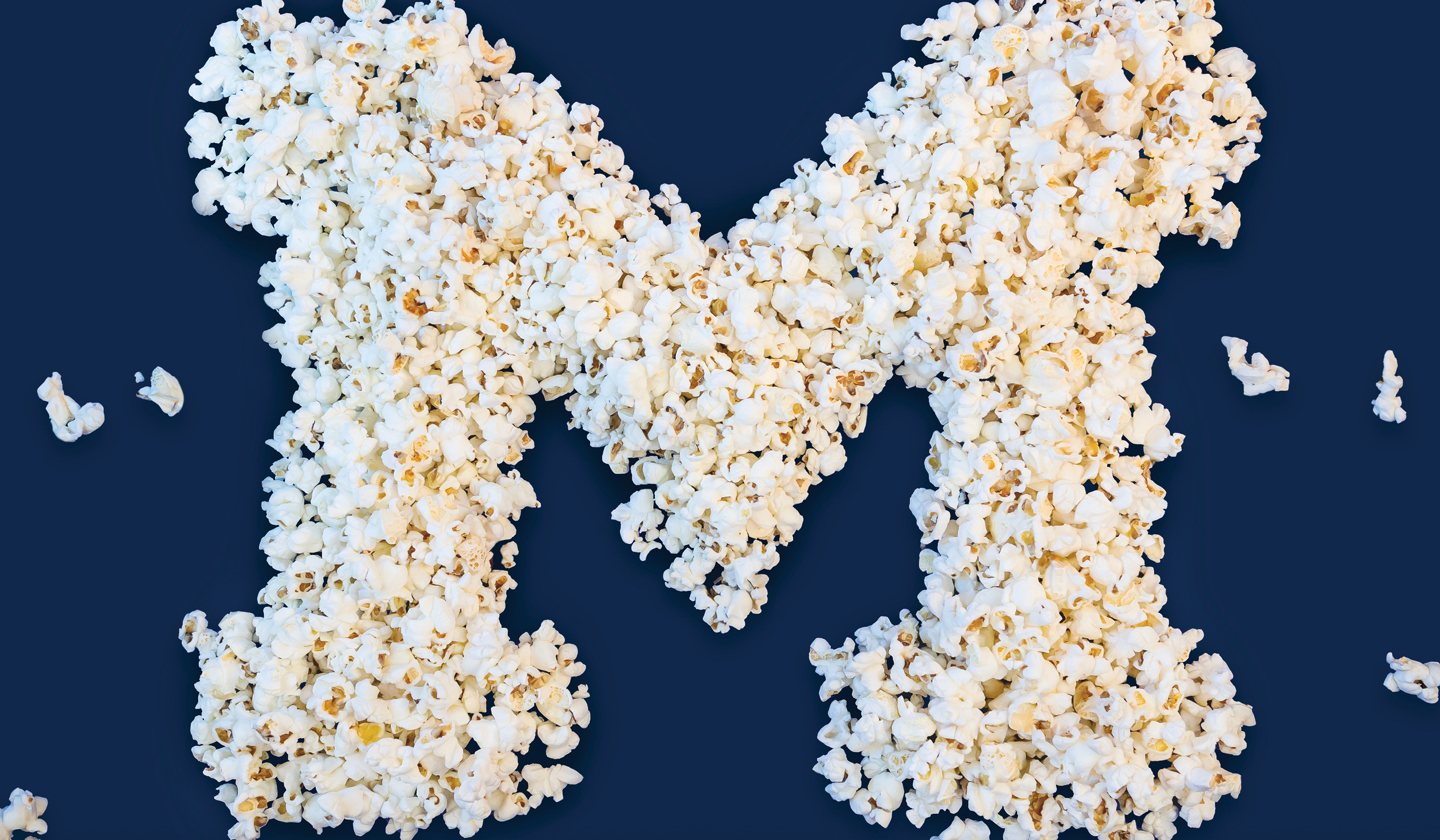 A pile of popcorn shaped into a block M with pieces of popcorn scattered around.